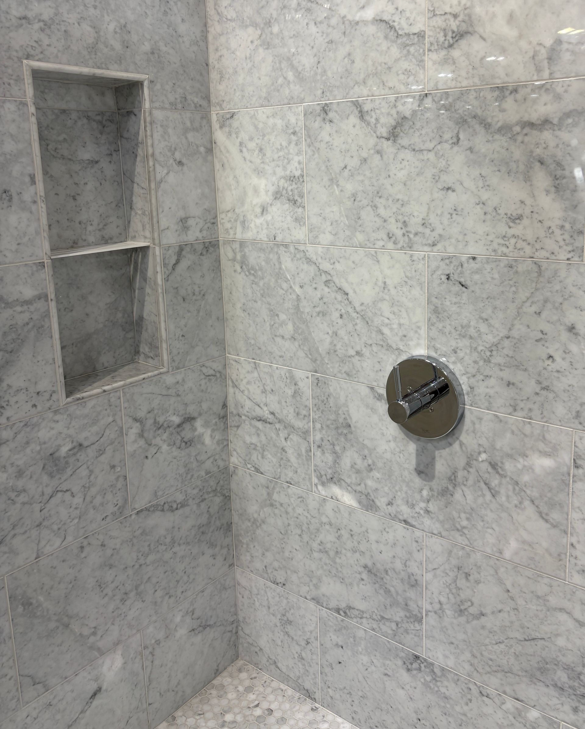 Marble-tiled shower interior with a built-in shelf and a silver faucet.