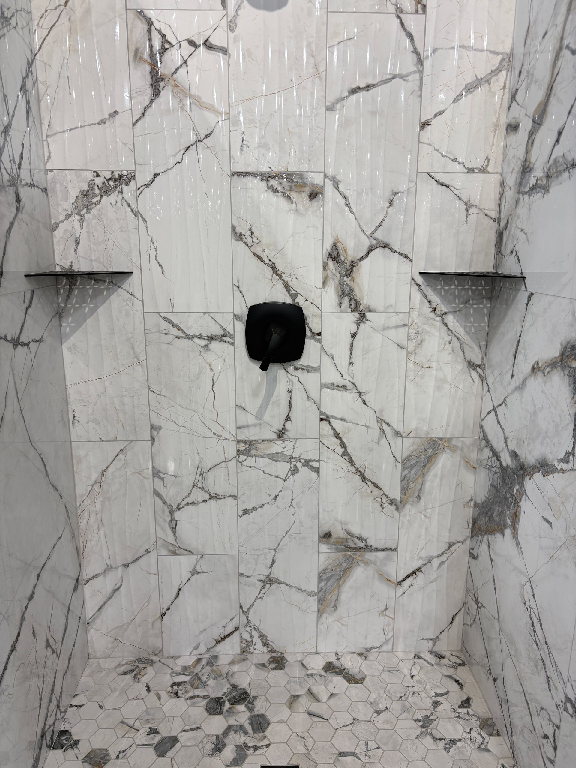 Marble-tiled shower with black fixtures and shelves; the walls feature gray veining.