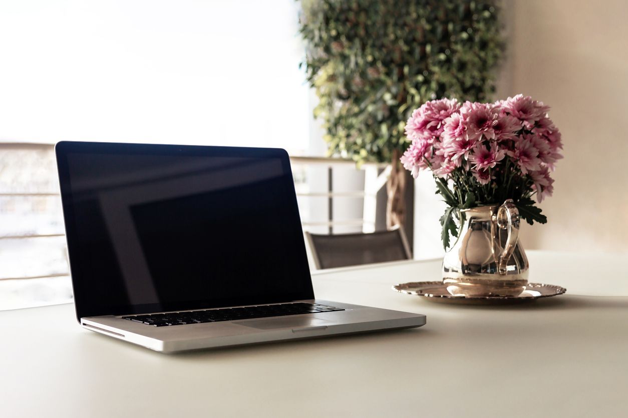 A laptop computer is sitting on a table next to a vase of pink flowers.