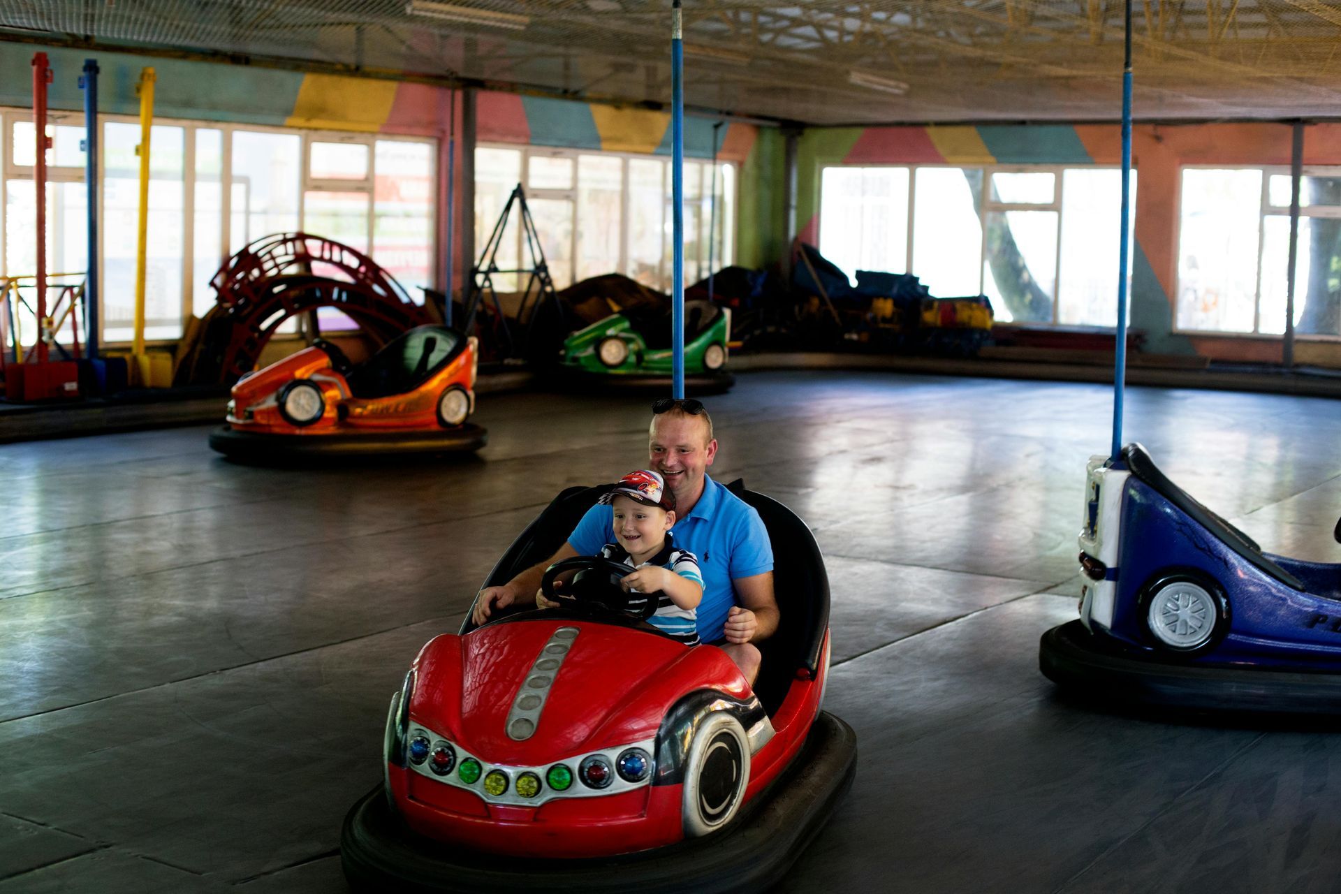 Man and child ride a red bumper car in an indoor amusement park.