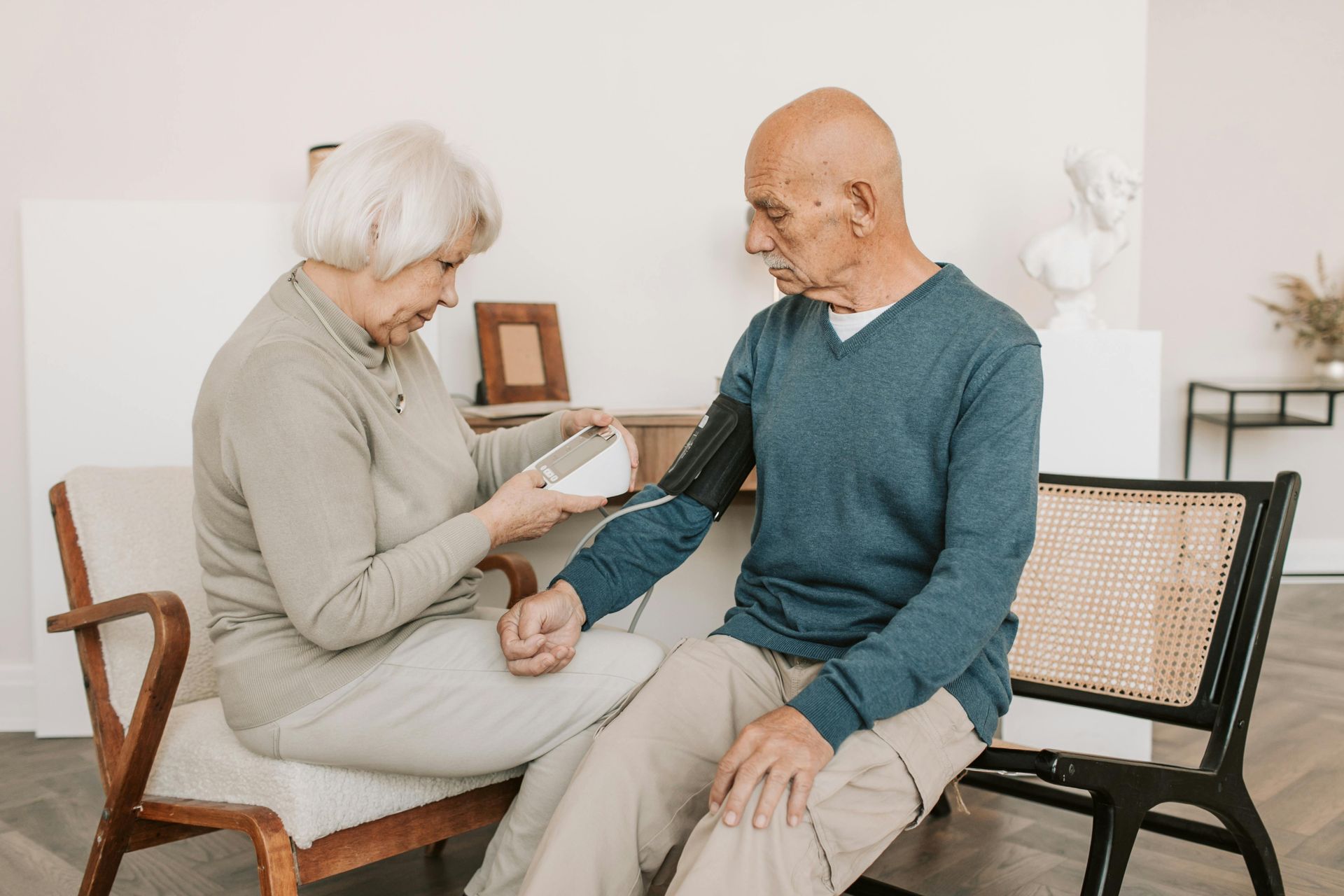 Woman taking man's blood pressure with an electronic monitor. They sit in a light-filled room.