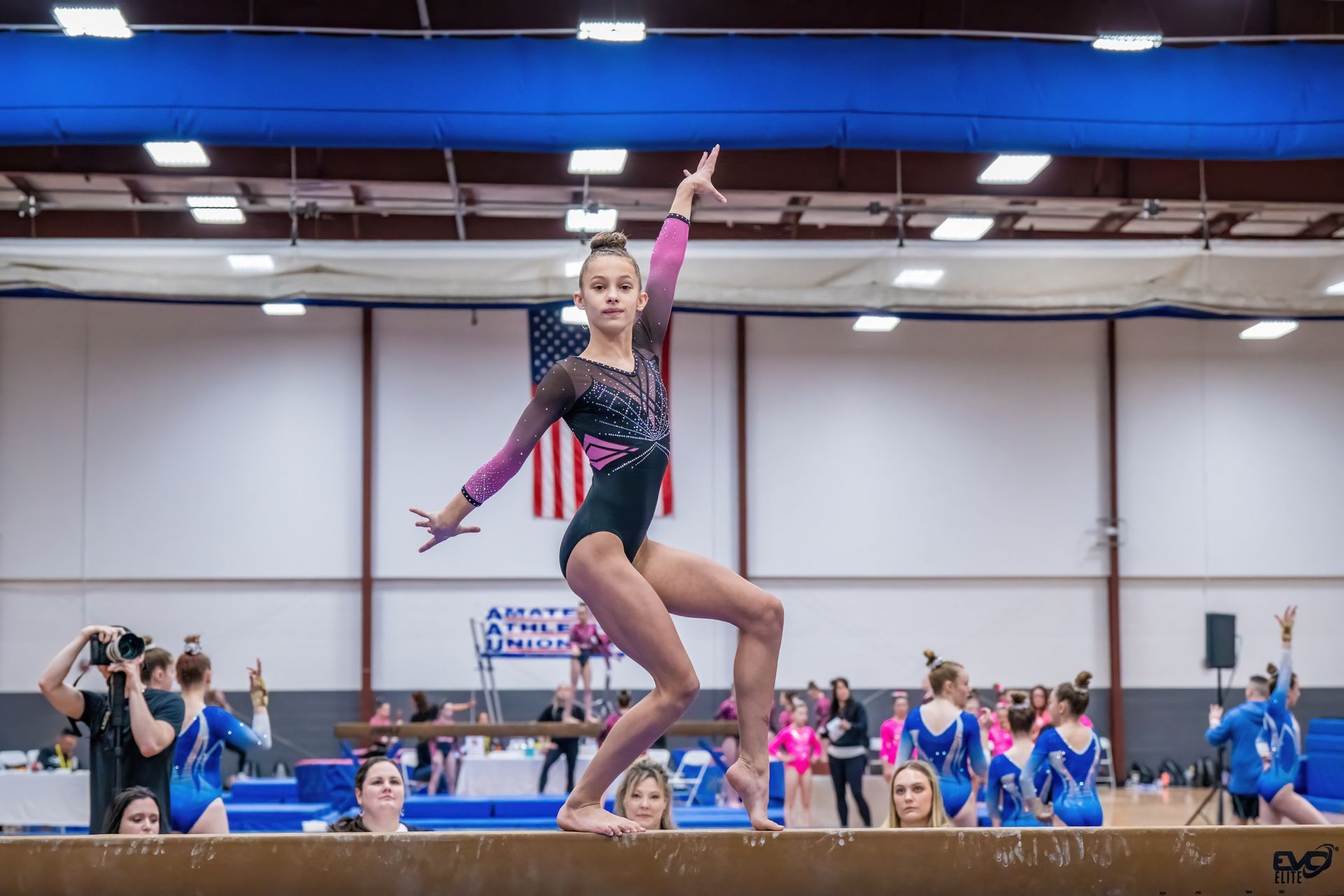 A young girl is standing on a balance beam in a gym.
