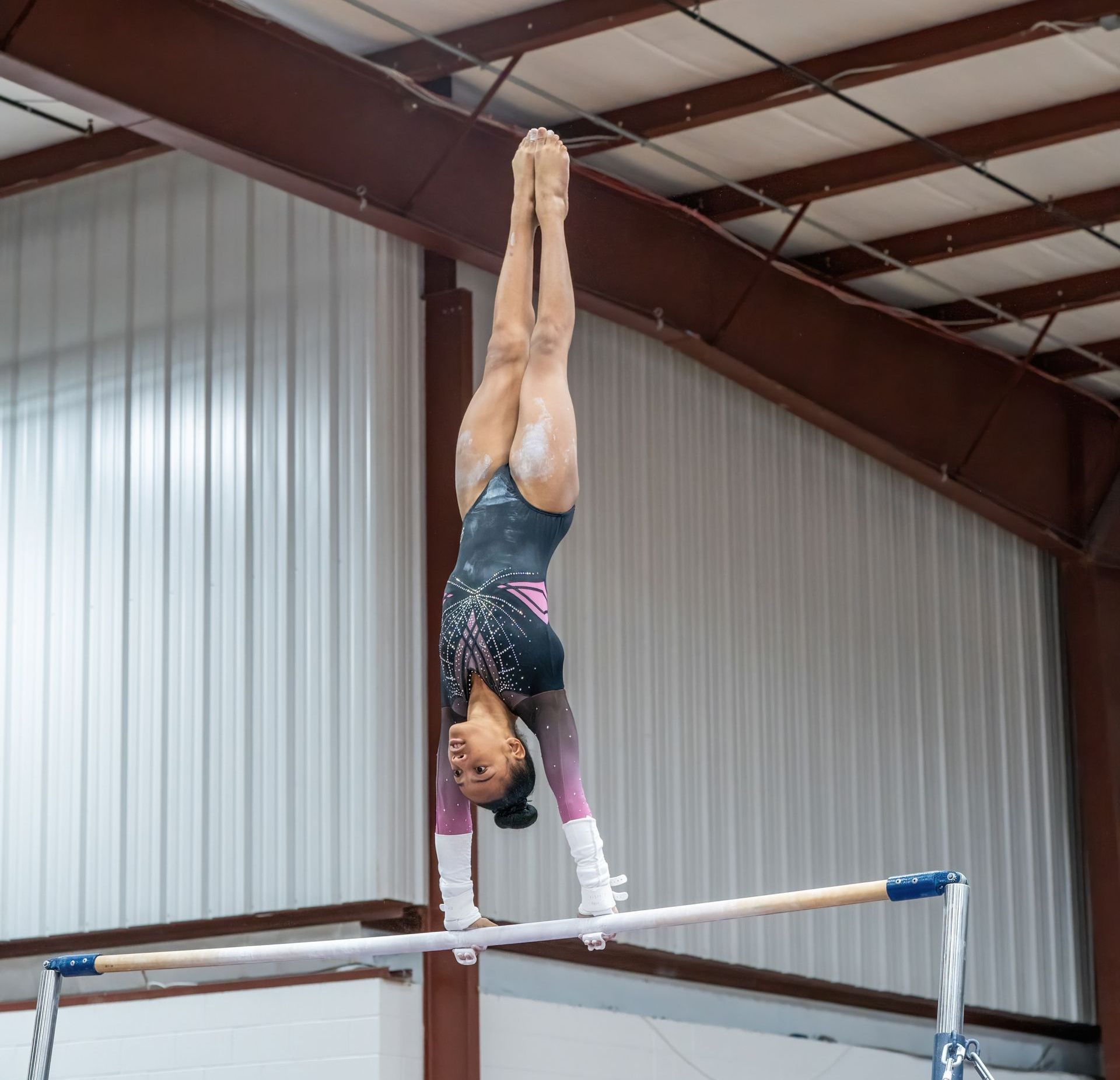 A female gymnast is doing a handstand on a parallel bars
