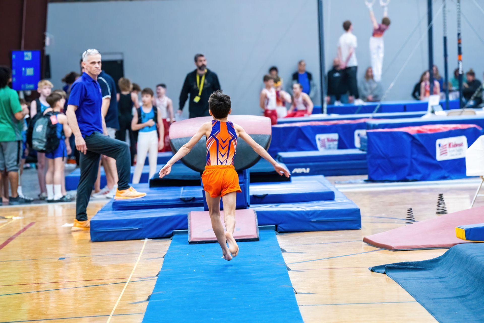 A young boy is jumping on a blue mat in a gym.