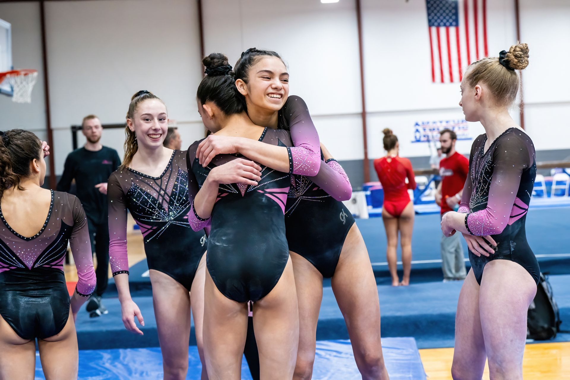 A group of female gymnasts are hugging each other in a gym.