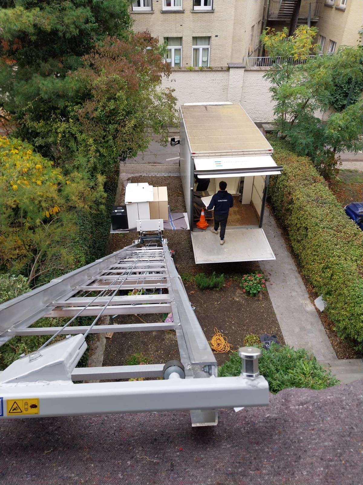 Camion blanc avec un bras de levage allongé à côté d'un bâtiment, probablement pour le déménagement.