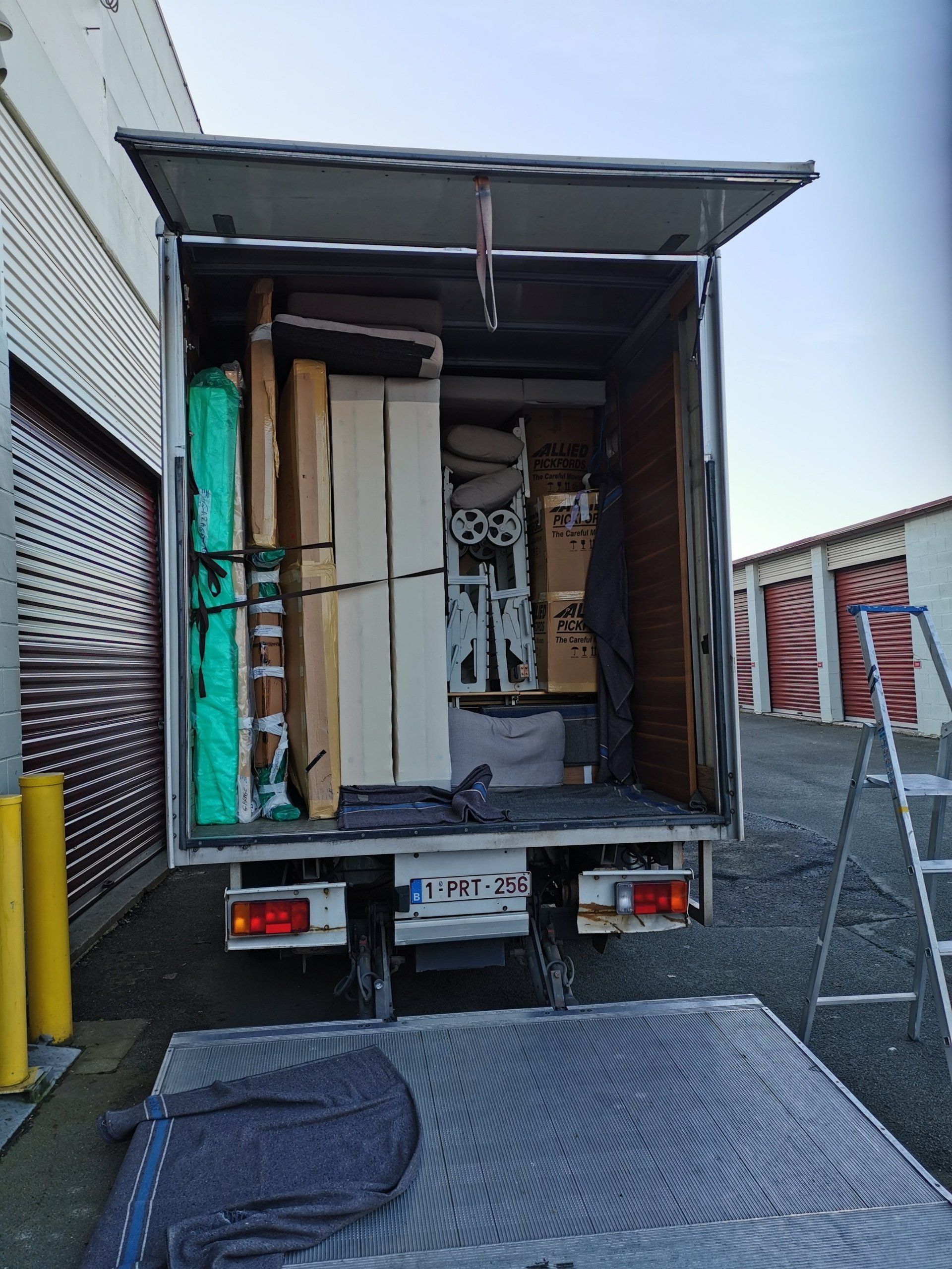 Plateforme de camion chargée de meubles dans un entrepôt ; rembourrage de protection bleu posé sur la rampe.