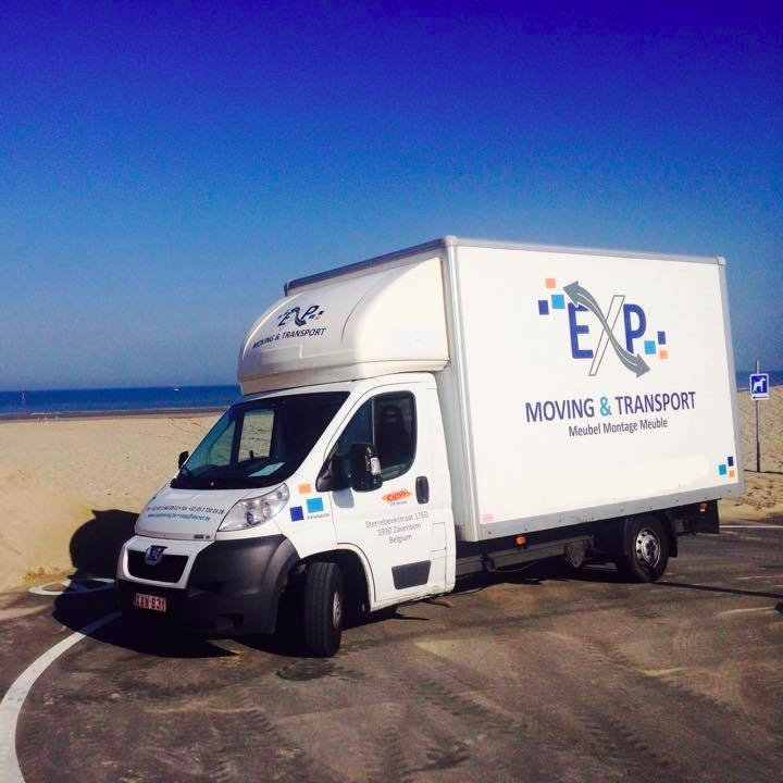 Camion de déménagement blanc avec le logo « EXP Moving & Transport » garé près d'une plage sous un ciel bleu.