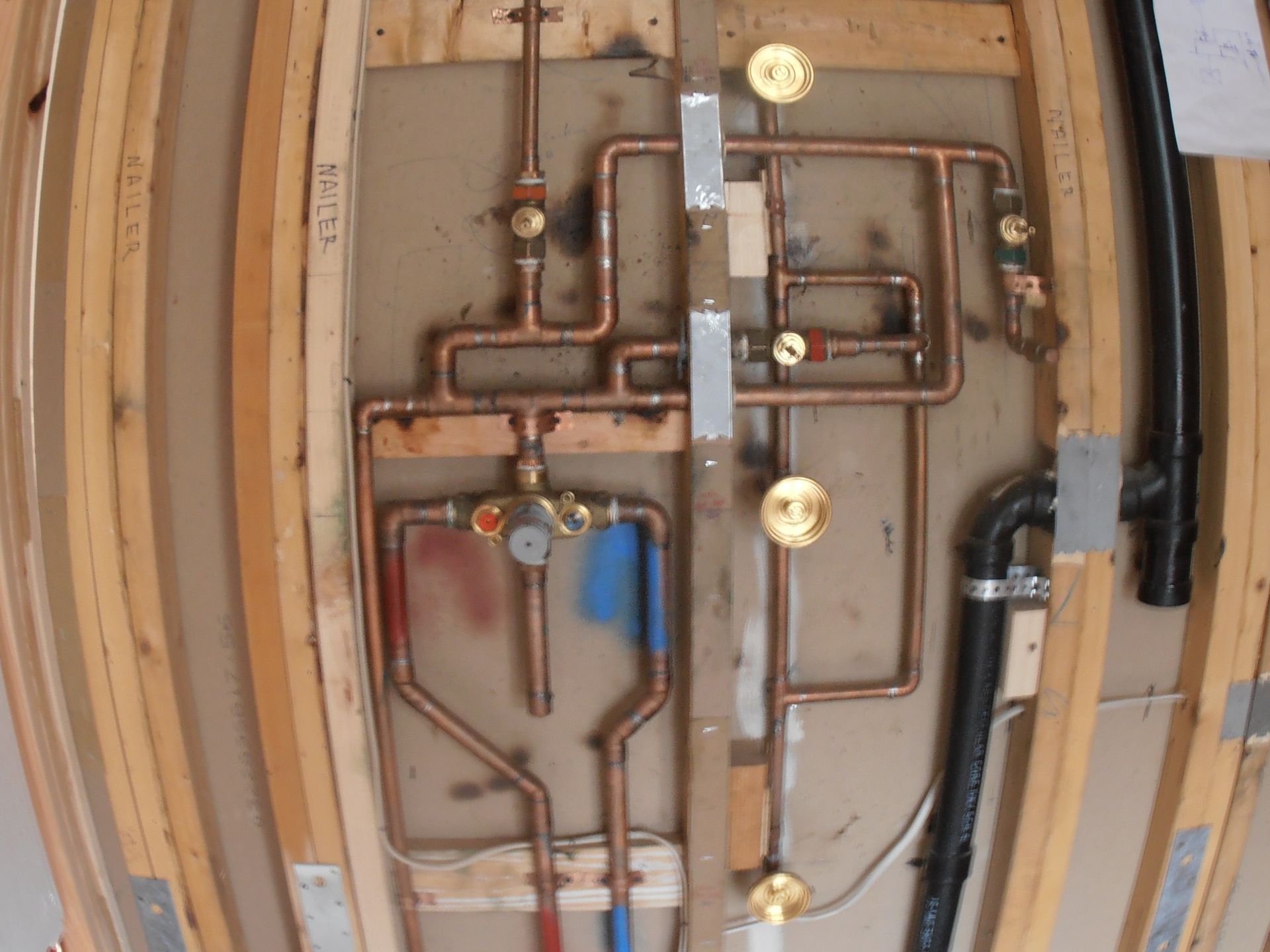 Copper plumbing pipes and a shower mixing valve installed inside an open wood-framed wall cavity.