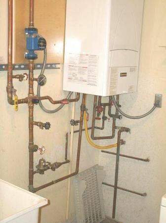 Wall-mounted white boiler with copper plumbing pipes, a blue pump, and yellow gas line in a utility room.