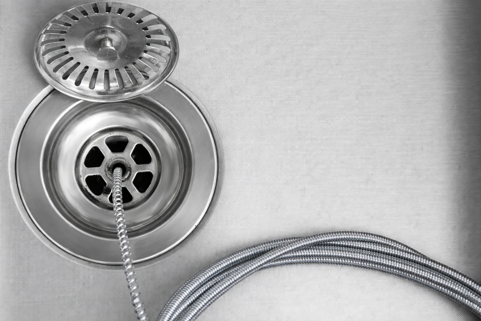 Person using a wrench to fix a leaking white pipe under a wooden shelf; water is spraying out.