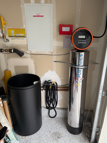 Utility room with water heater, black trash can, and electrical panel on a wall.