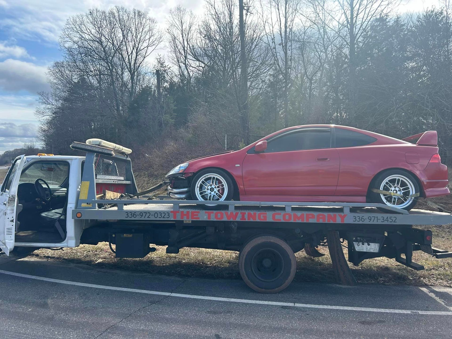 A red car is being towed by a tow truck.