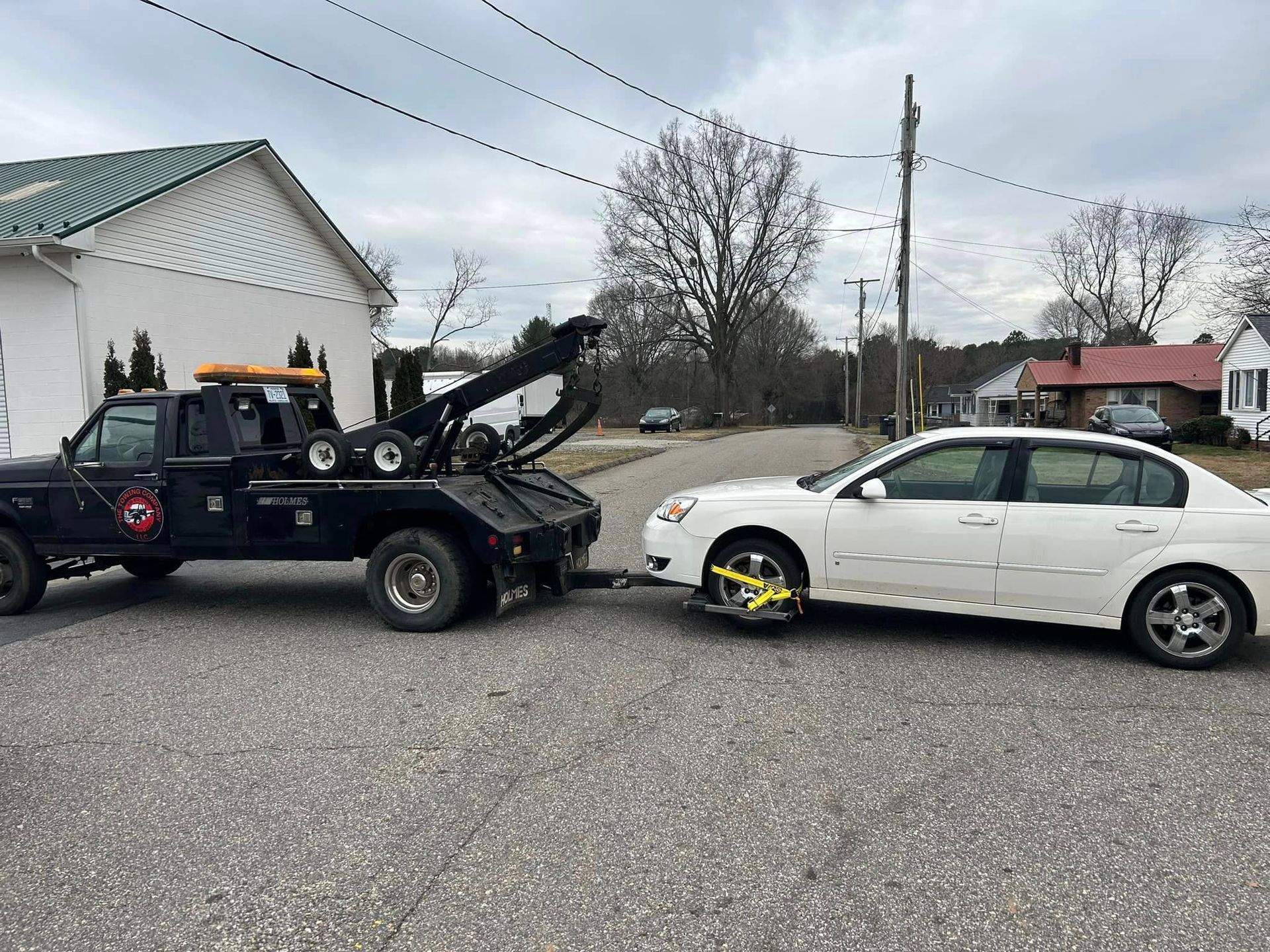 A white car is being towed by a tow truck.