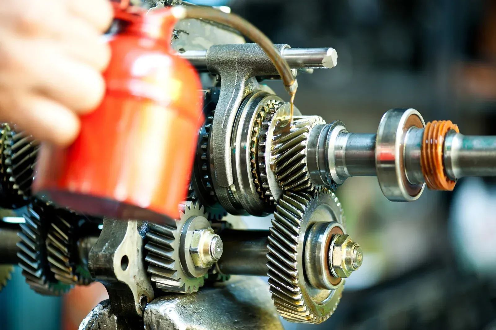 Person lubricating gears with an oil can, in an industrial setting.