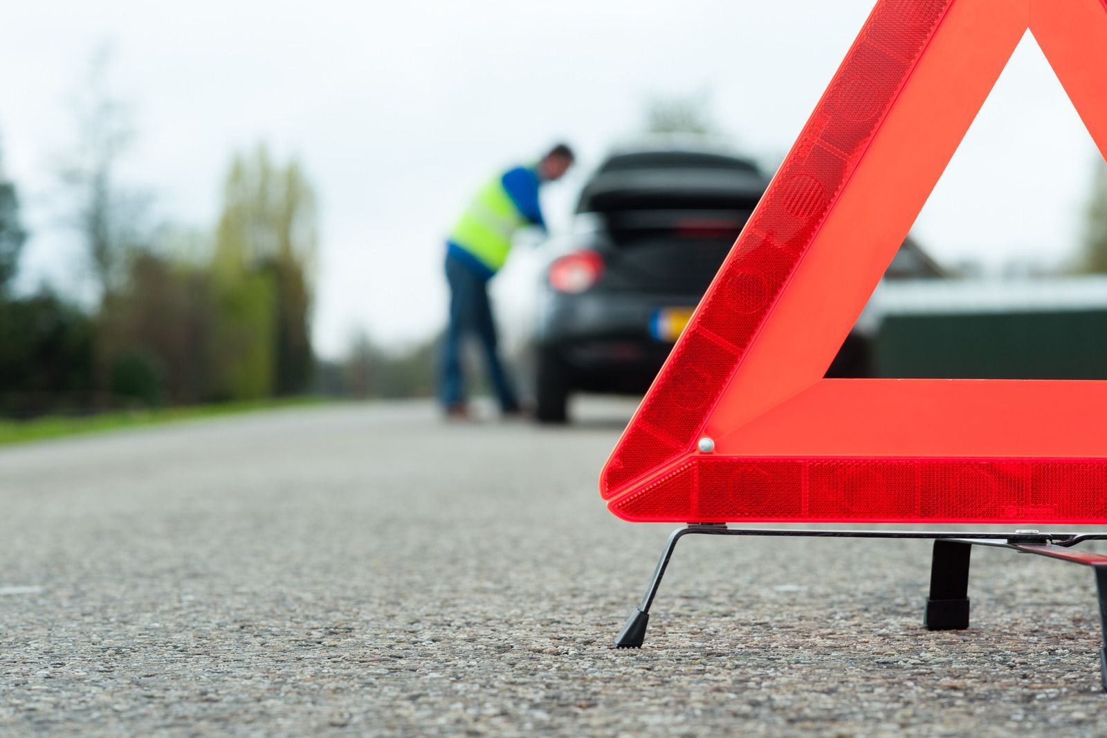 A man is standing next to a broken down car on the side of the road.
