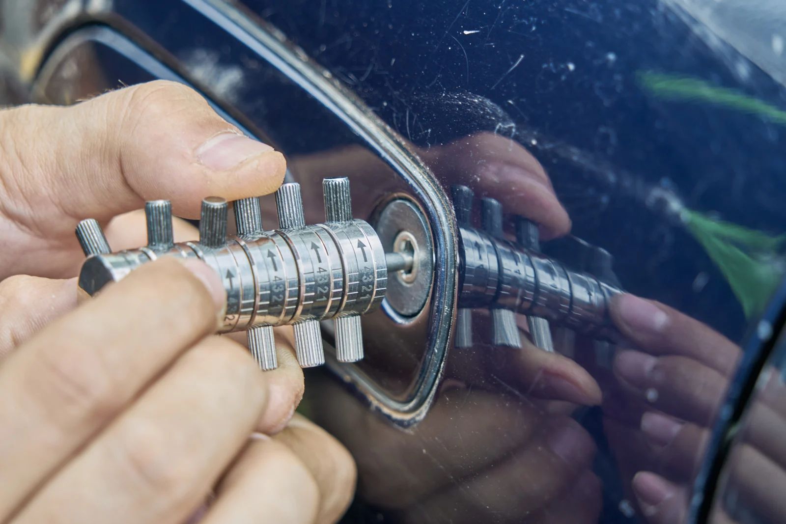 A person's hands using a lock pick to try to open a car door.