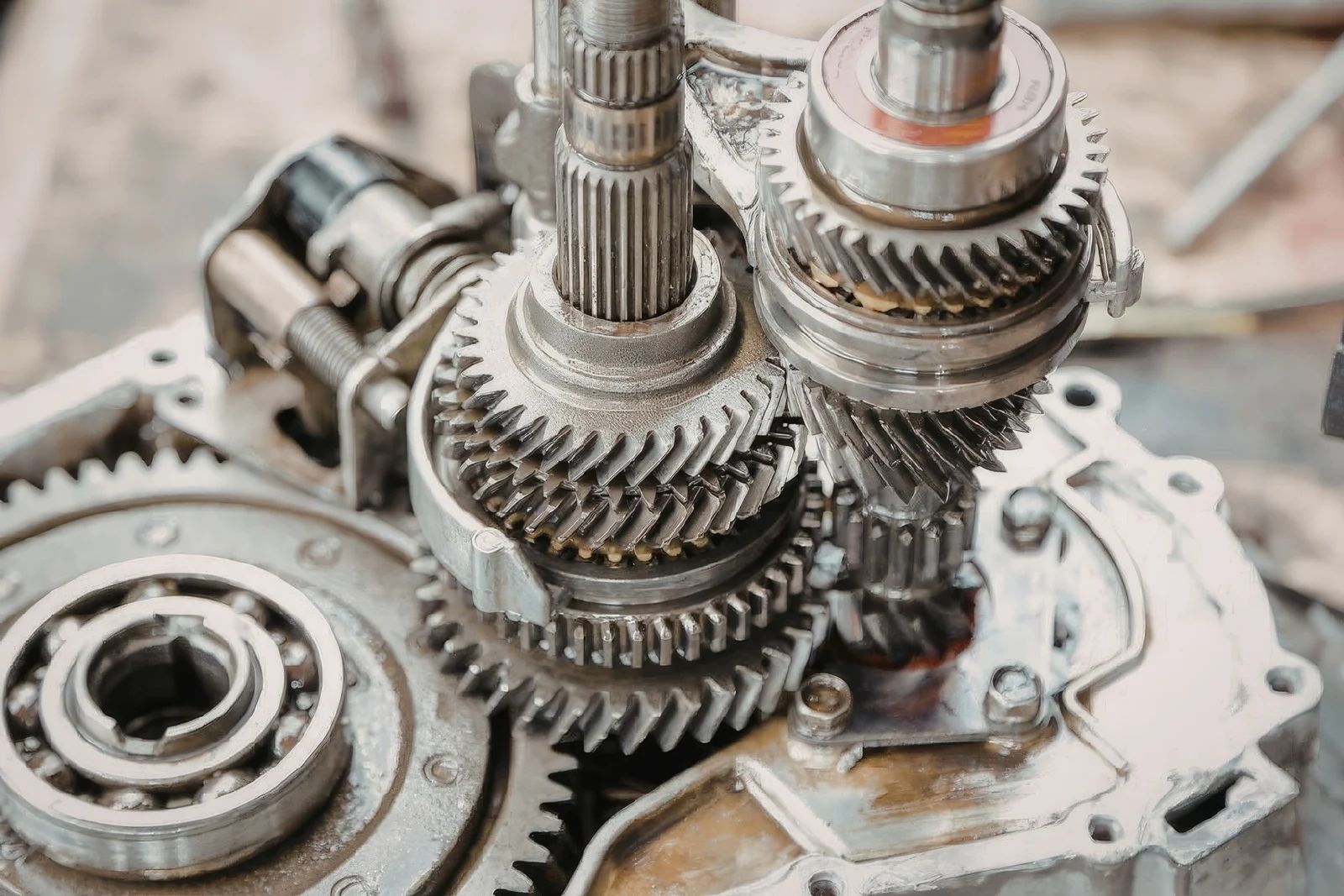 Close-up of a disassembled manual transmission, highlighting interlocking metal gears and drive shafts in a workshop.