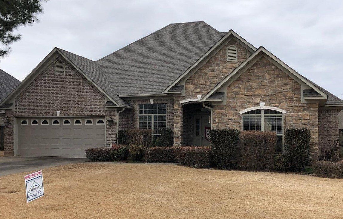 A large brick house with a garage and a sign in front of it.