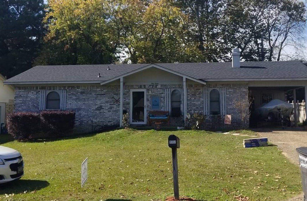 A white car is parked in front of a brick house.