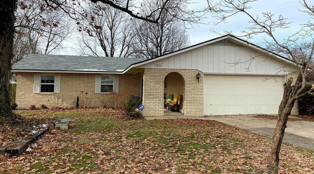 A house with a white garage door is surrounded by trees and leaves.
