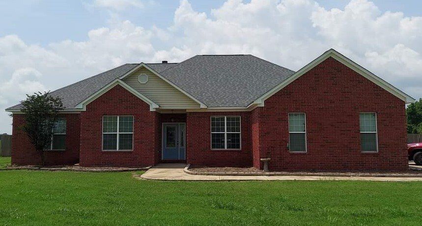 A large red brick house with a gray roof is sitting on top of a lush green field.