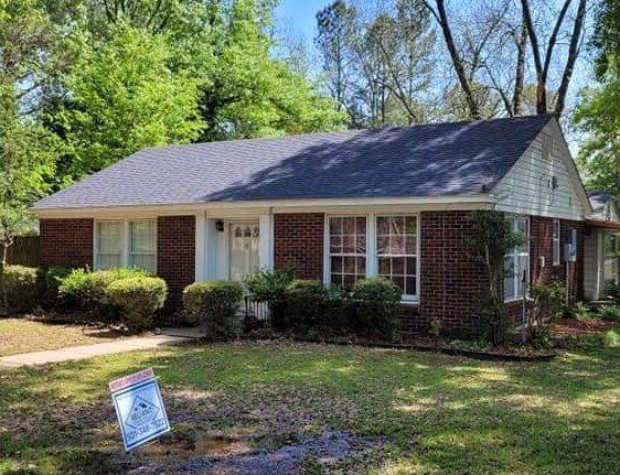 A brick house with a gray roof and a for sale sign in front of it.