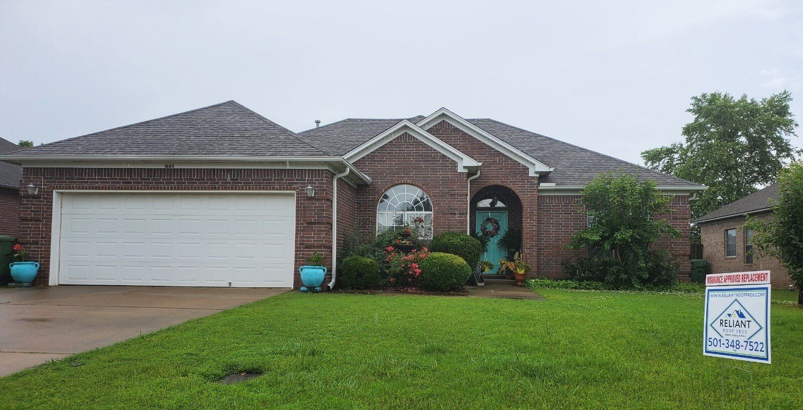 A brick house with a white garage door and a sign in front of it