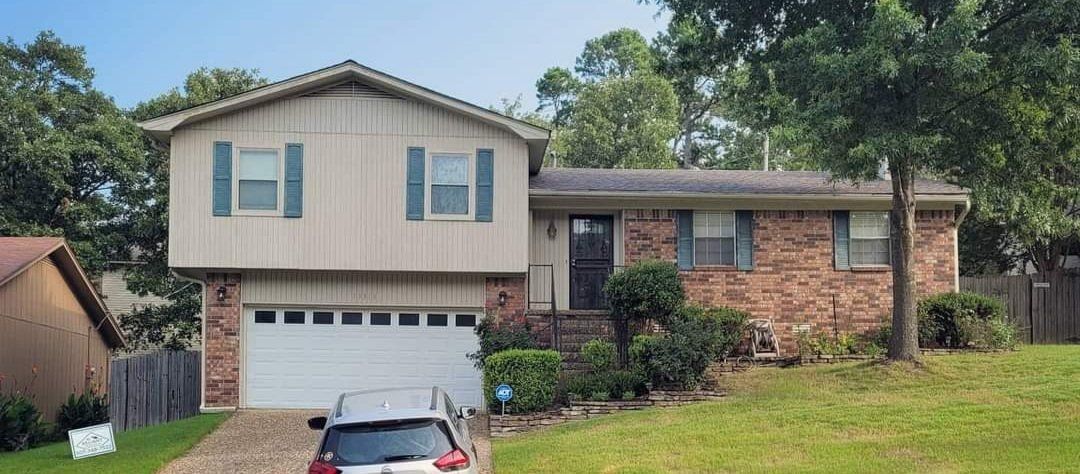 A car is parked in front of a brick house with a garage.