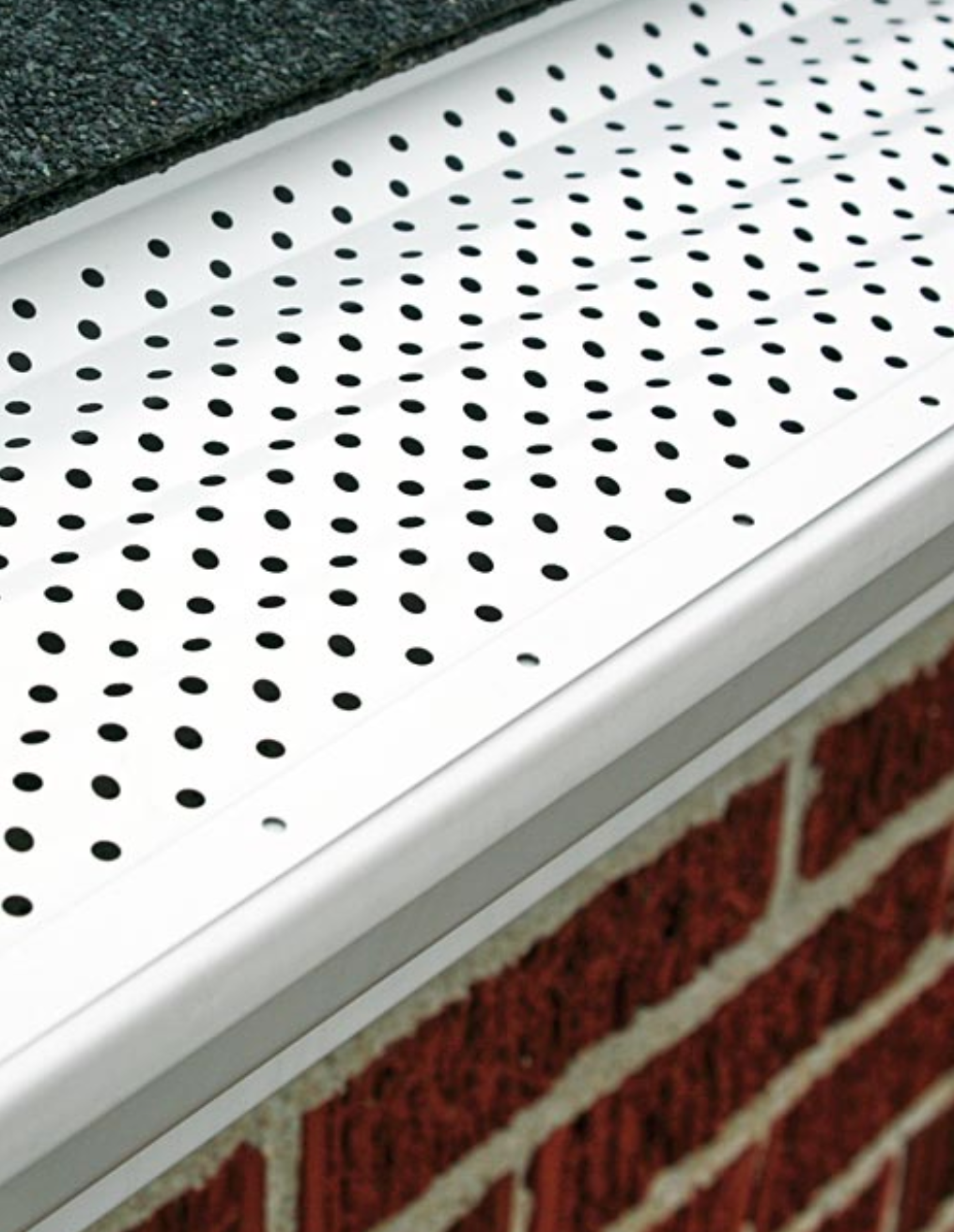A gutter with holes in it is on a brick wall