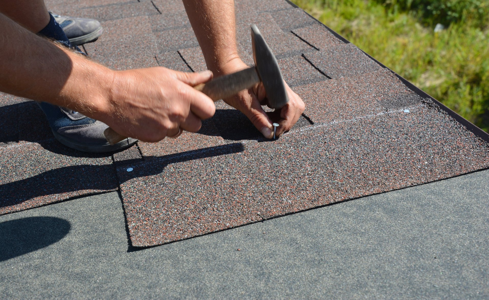A man is hammering a nail into a roof with a hammer.