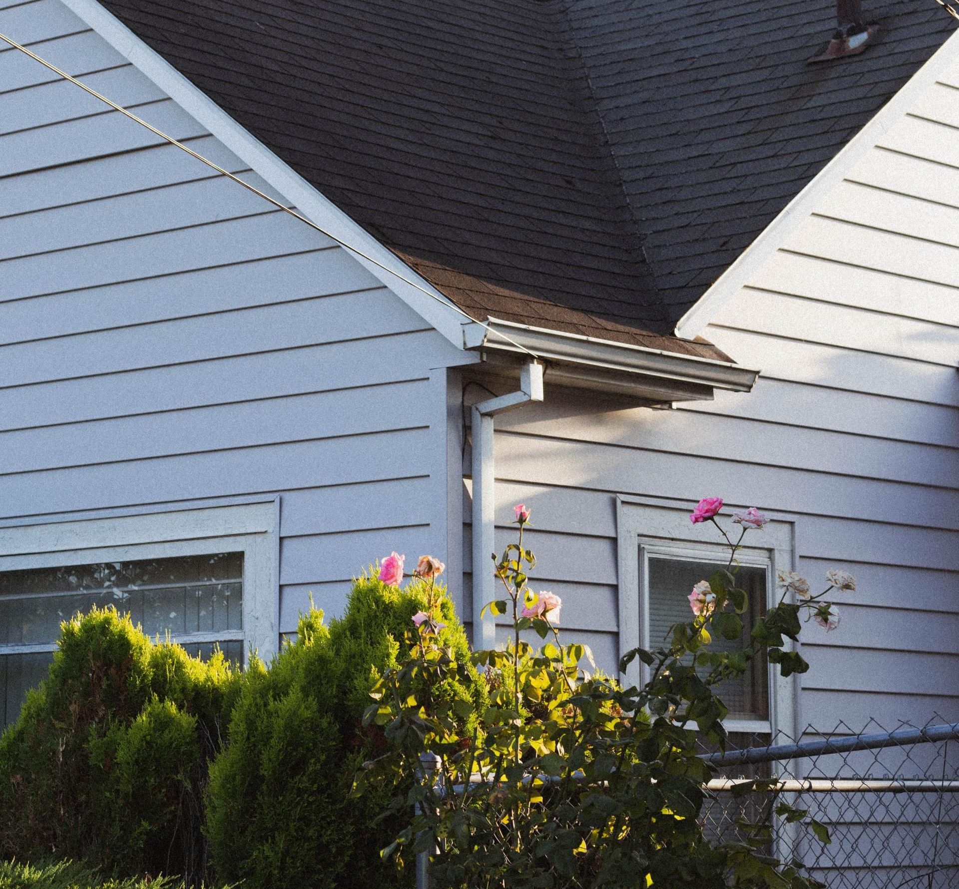 A white house with a black roof and pink flowers in front of it