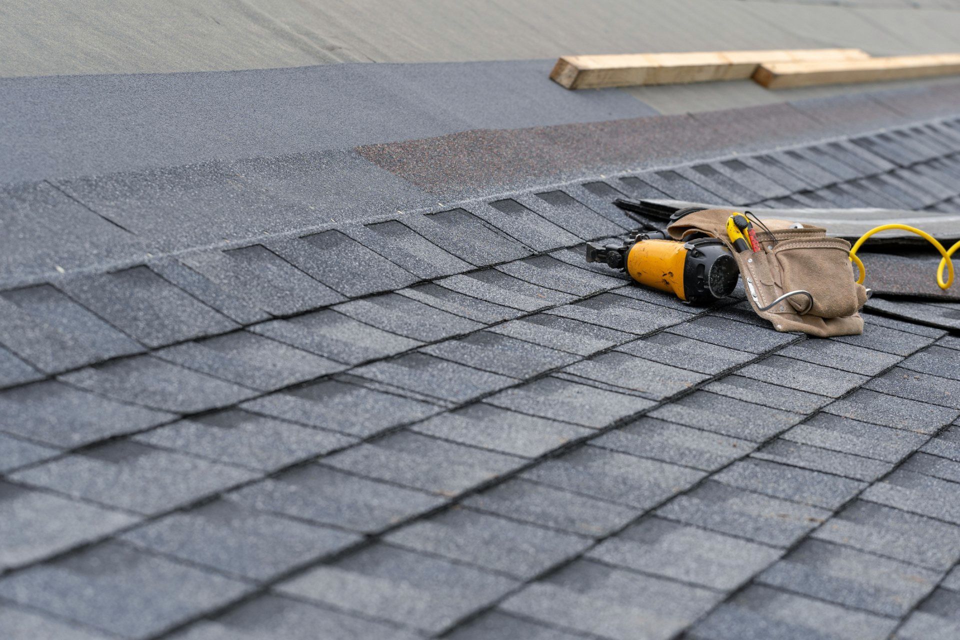 A roof with shingles being installed and tools on it.