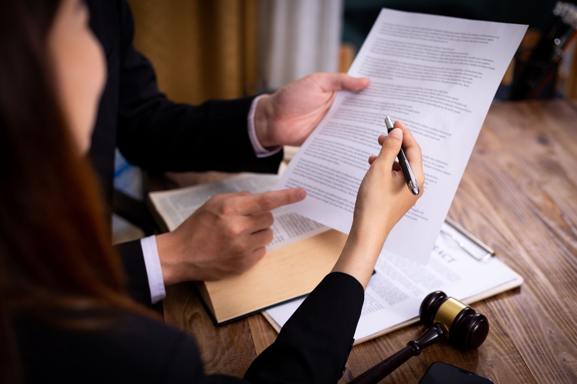 Two people review a document at a desk, with one pointing and the other signing with a pen.