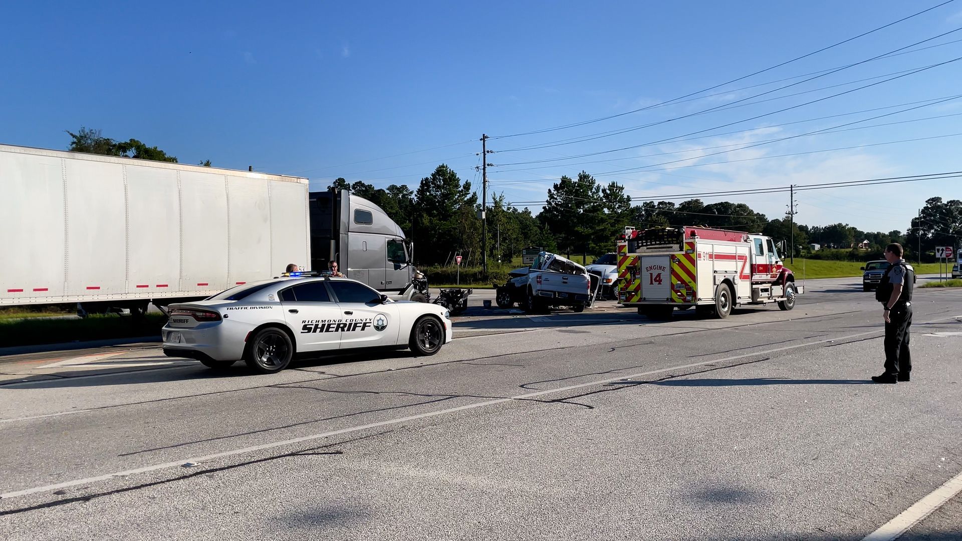 Police cars and an ambulance block a highway after a crash, with a truck and scattered debris nearby.