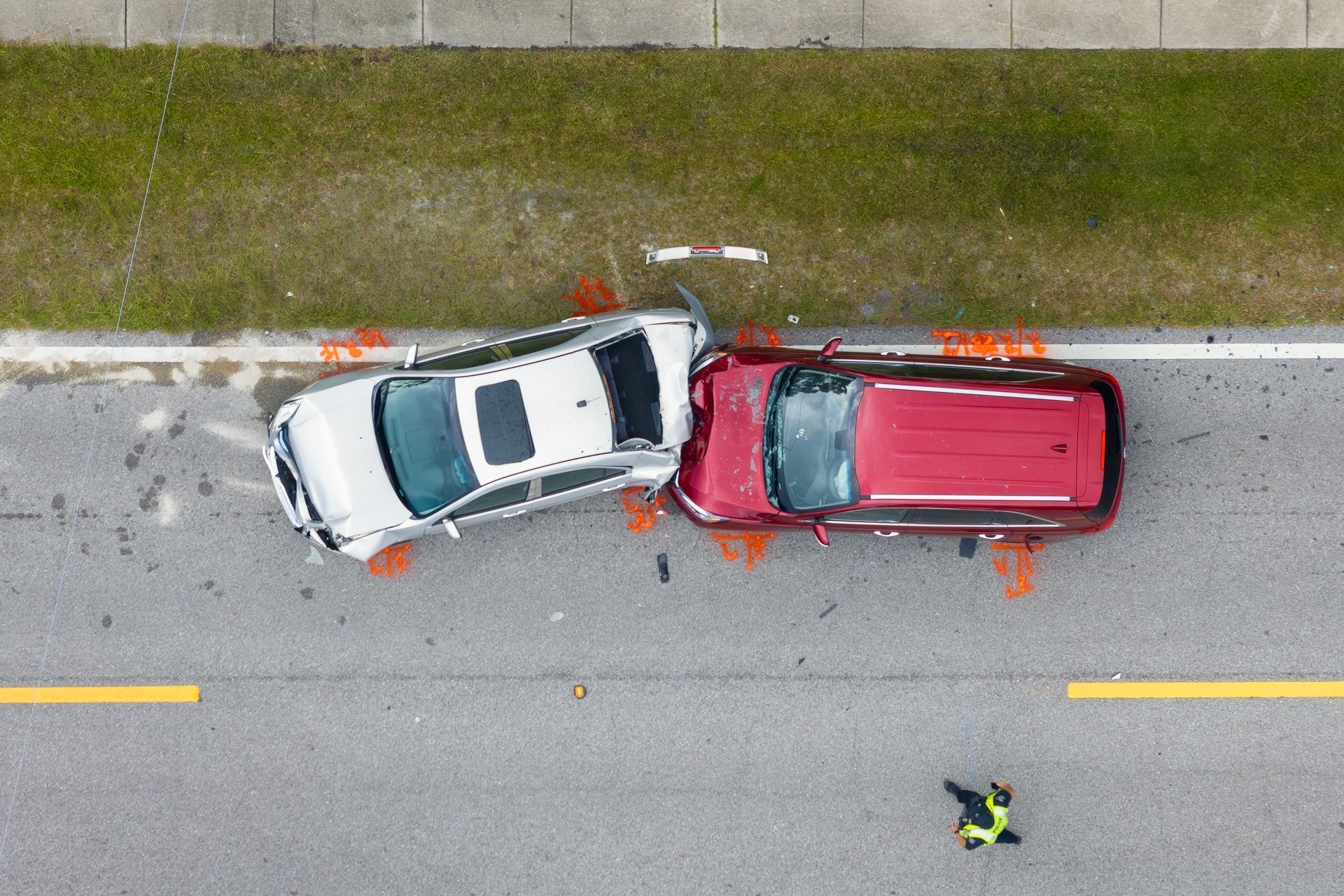 Overhead view of a white SUV and red minivan in a roadside collision, with debris and a person nearby