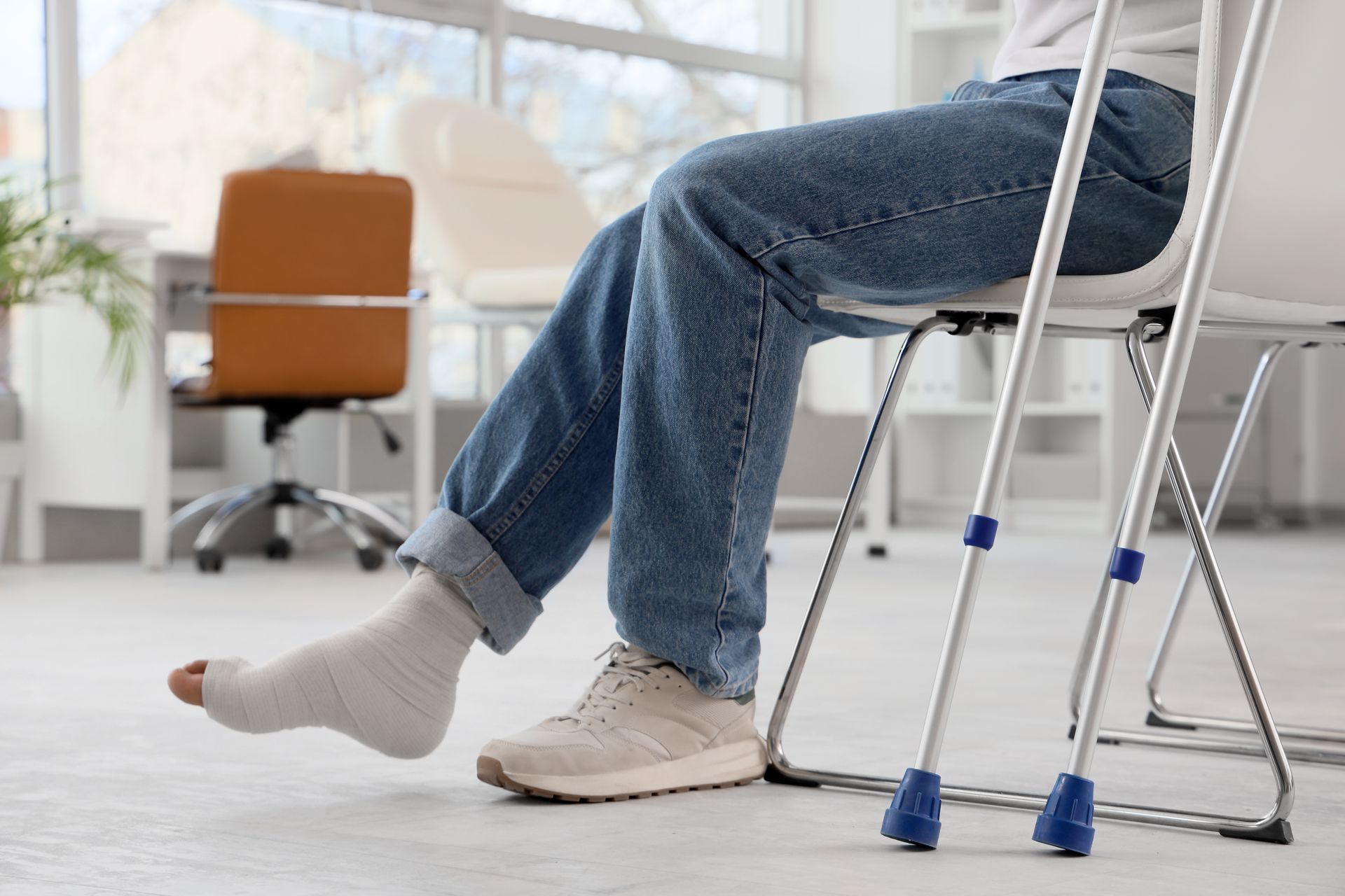 Person with a leg cast sits on a chair using crutches in a bright office.