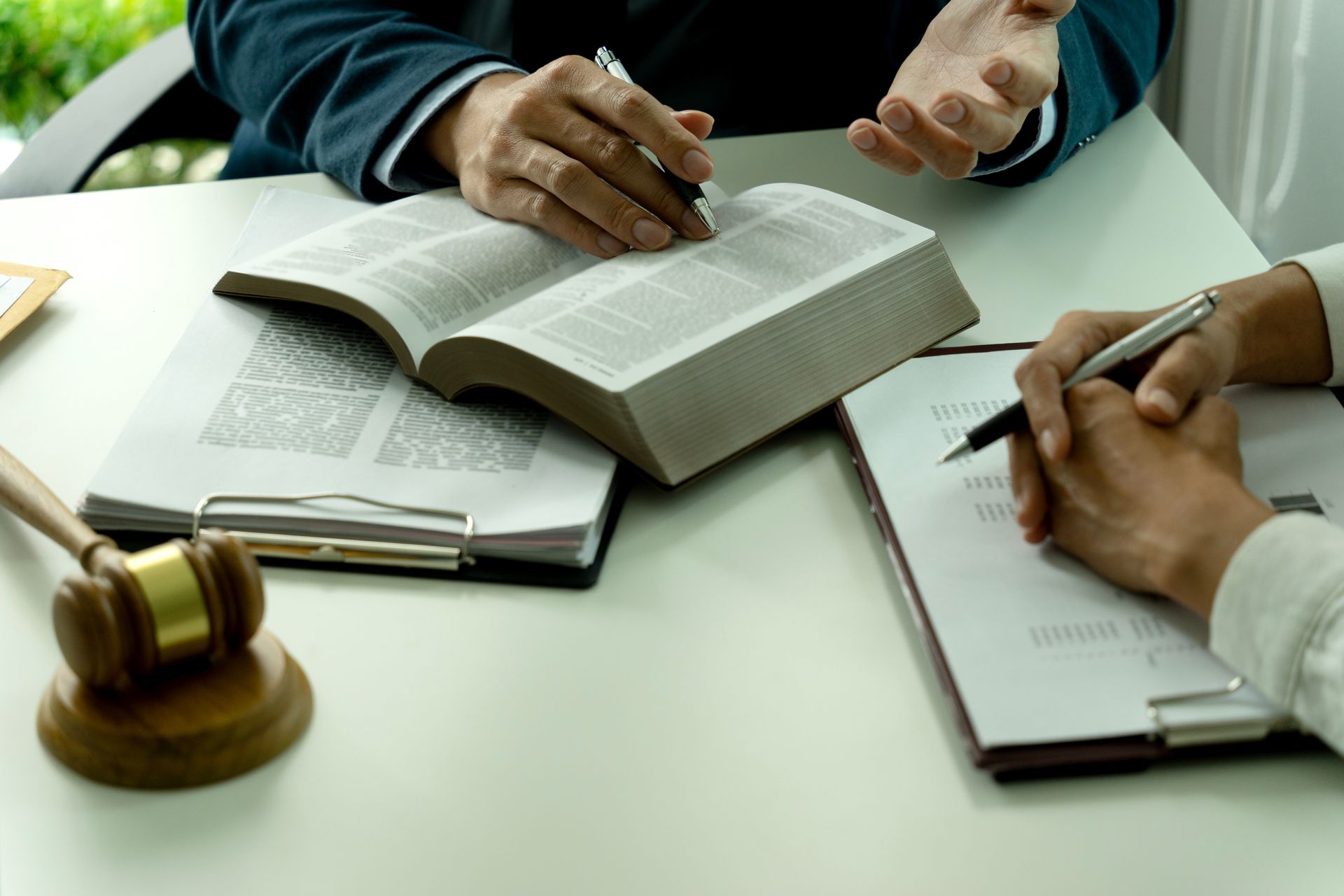 Lawyer’s desk with open book, gavel, and two people taking notes during a meeting