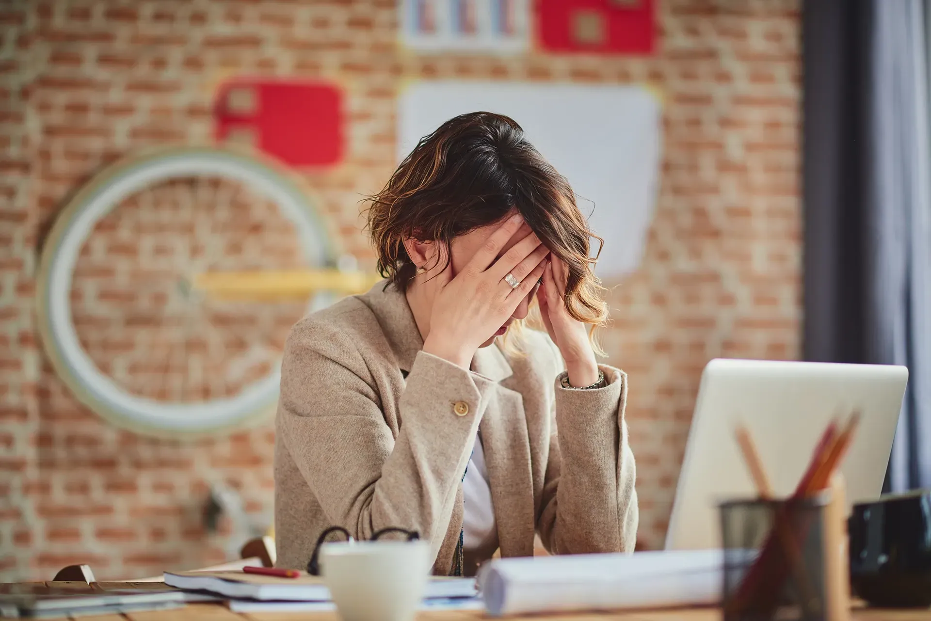 A woman is sitting at a desk with her head in her hands.