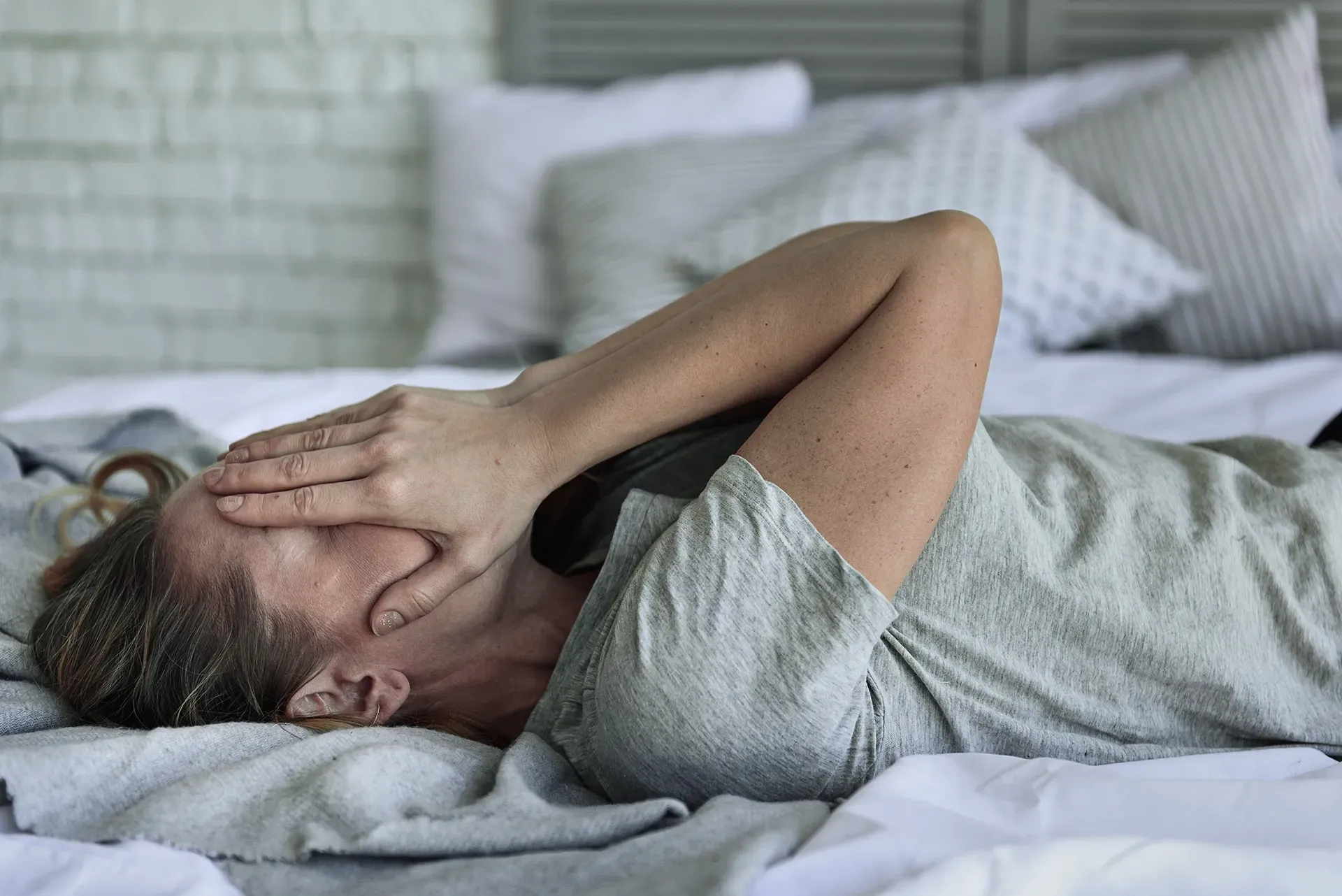 A woman is laying on a bed with her hand on her face.