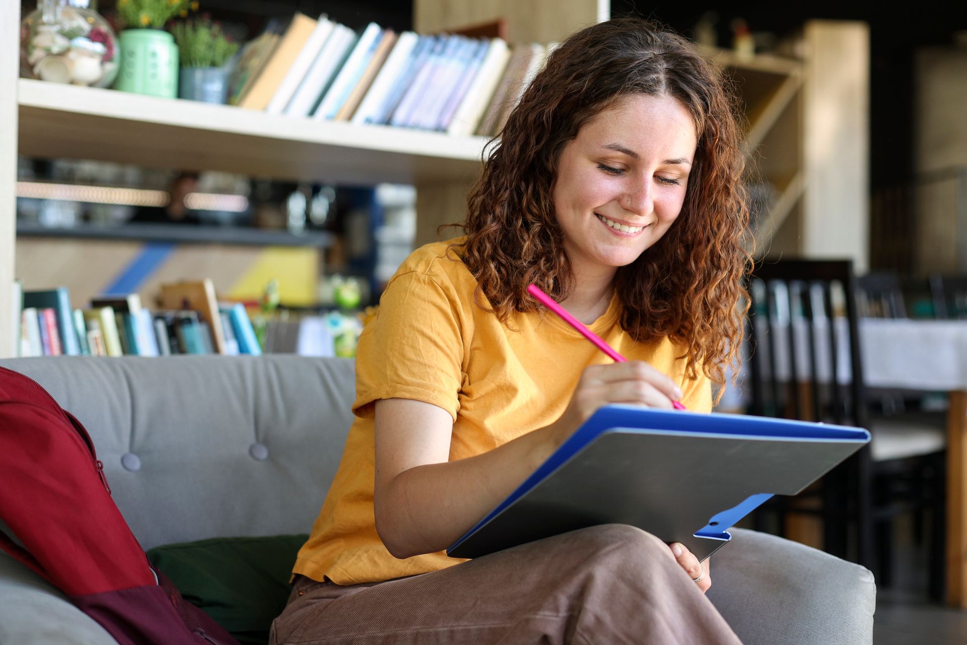 Woman with curly hair smiles while writing in a binder.