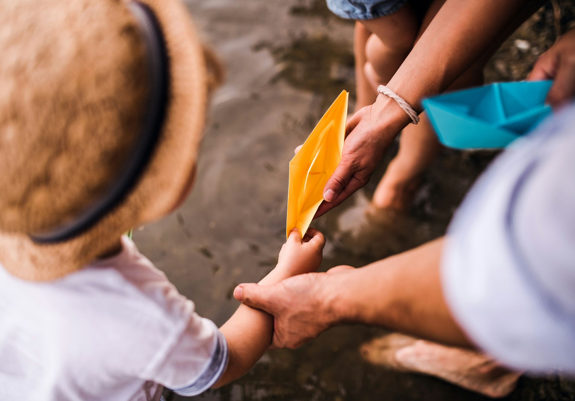 A family is playing with a paper boat in the water.