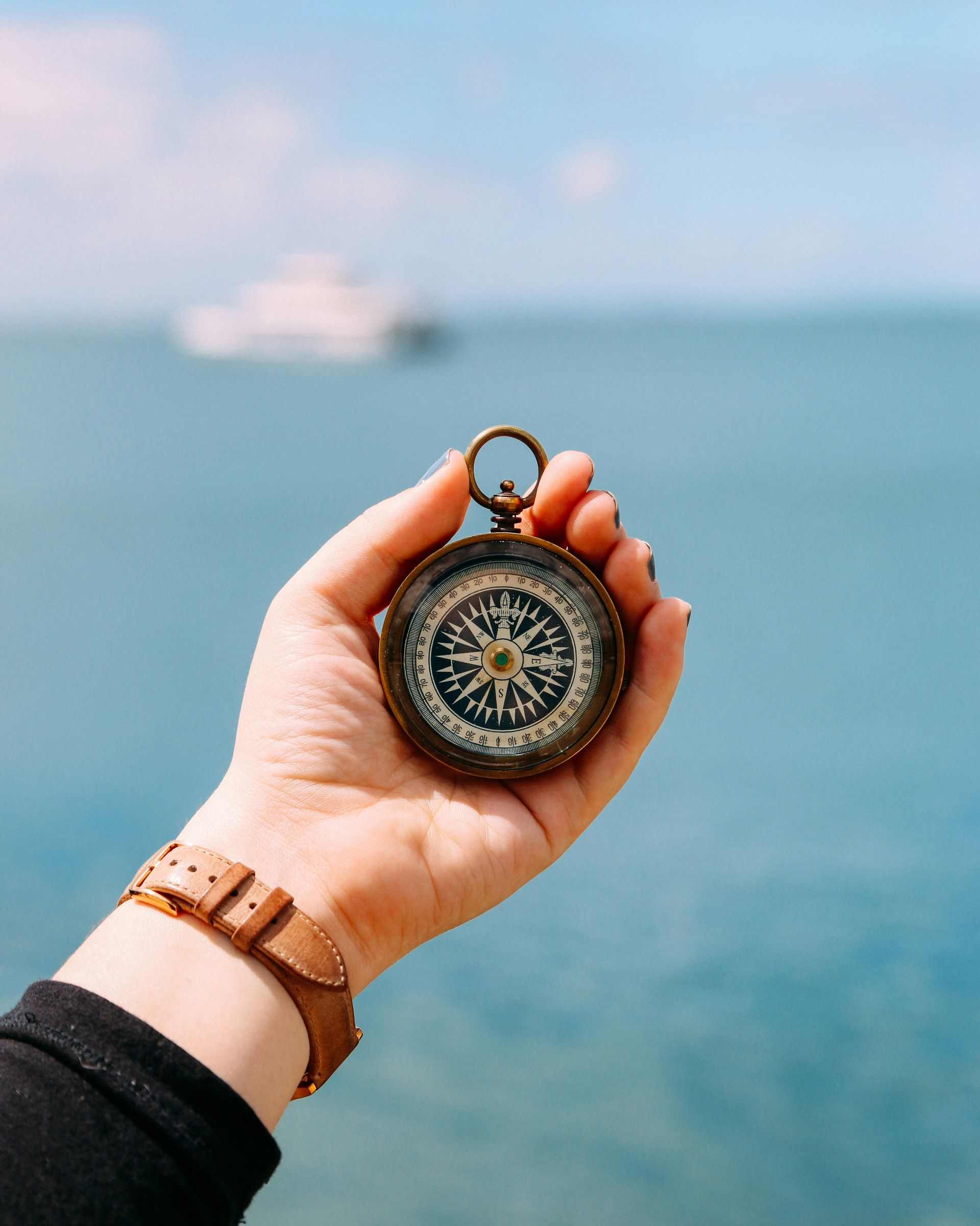 A person is holding a compass in their hand in front of the ocean.