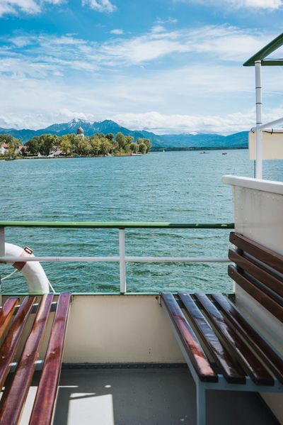 A wooden bench on the deck of a boat looking out over a lake.