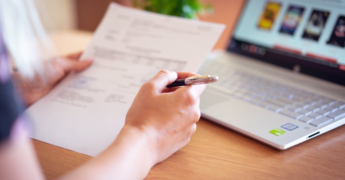 A person is writing on a piece of paper in front of a laptop computer.