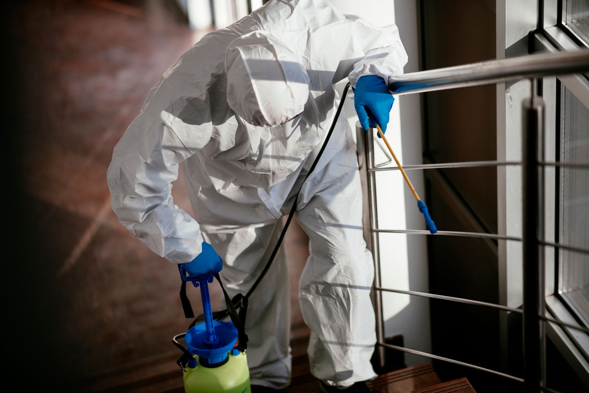 An exterminator wearing a protective suit is treating a residential stairwell. An exterminator wearing a protective suit is treating a residential stairwell.