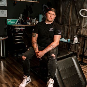 A man is sitting on a tattoo chair in a tattoo studio.