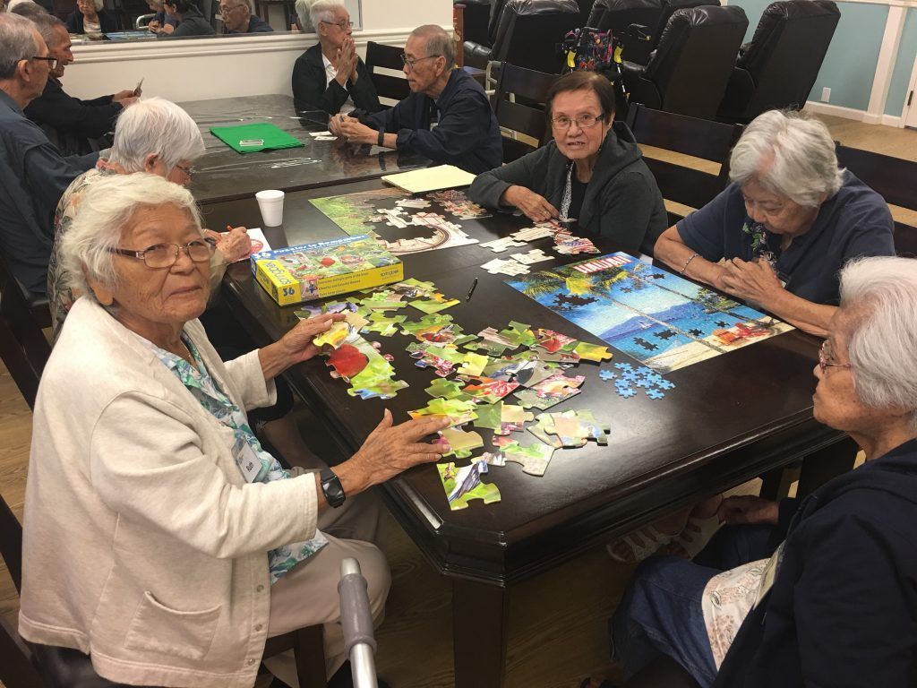 A group of elderly people are sitting around a table playing a game of puzzles.