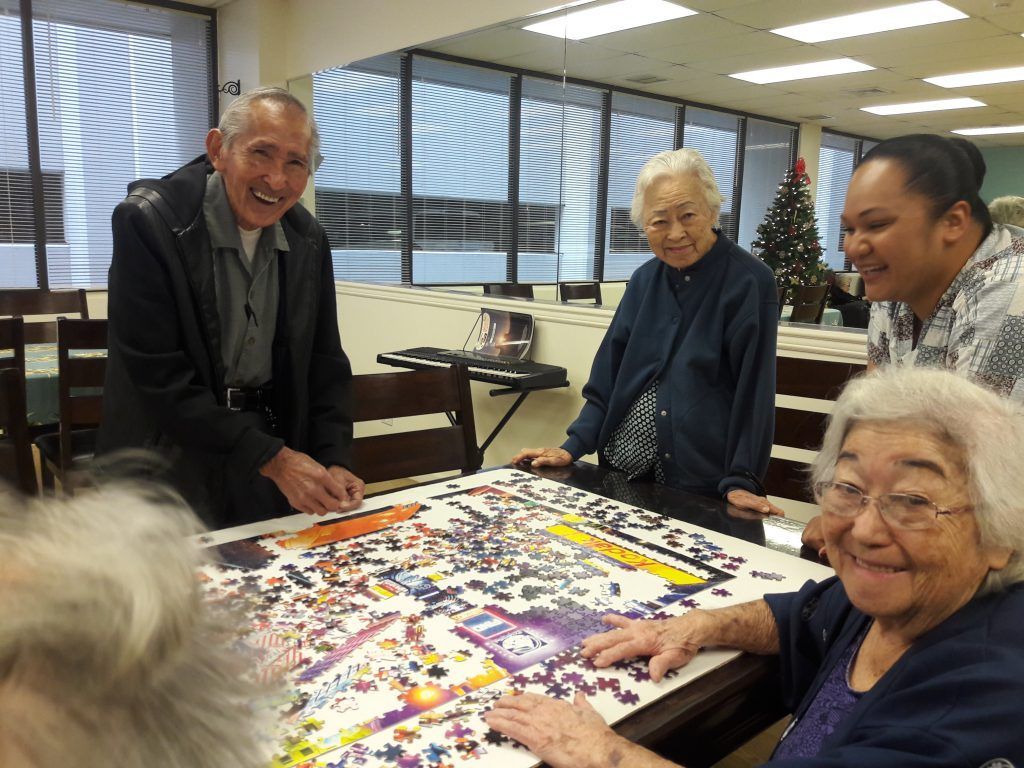 A group of people are sitting around a table doing a puzzle.