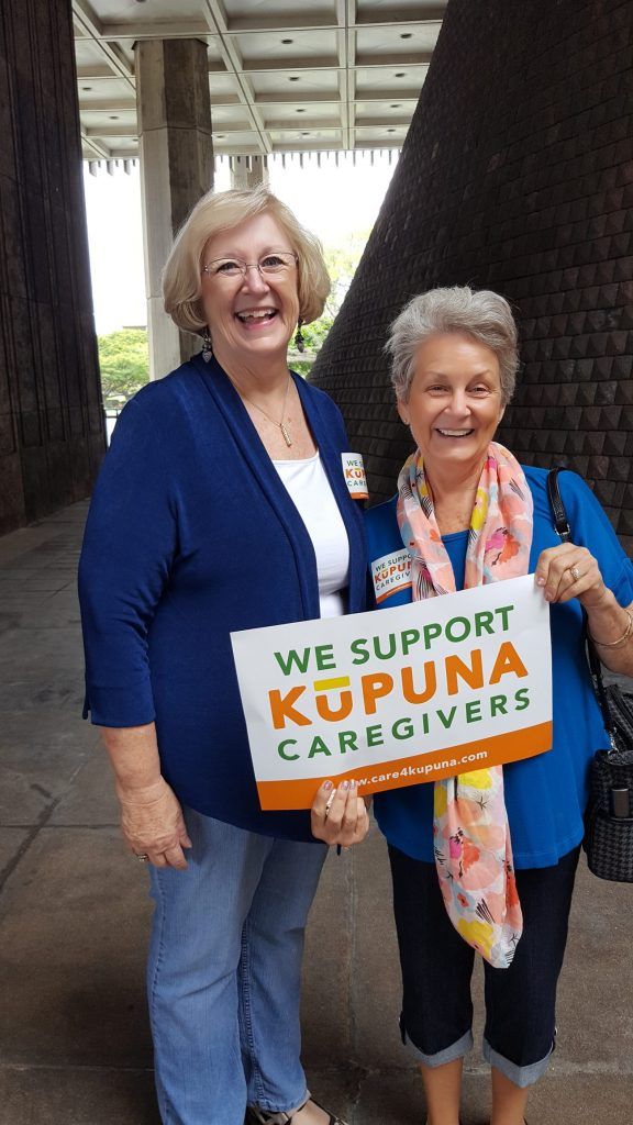 Two women are standing next to each other holding a sign that says `` we support kupuna caregivers ''.